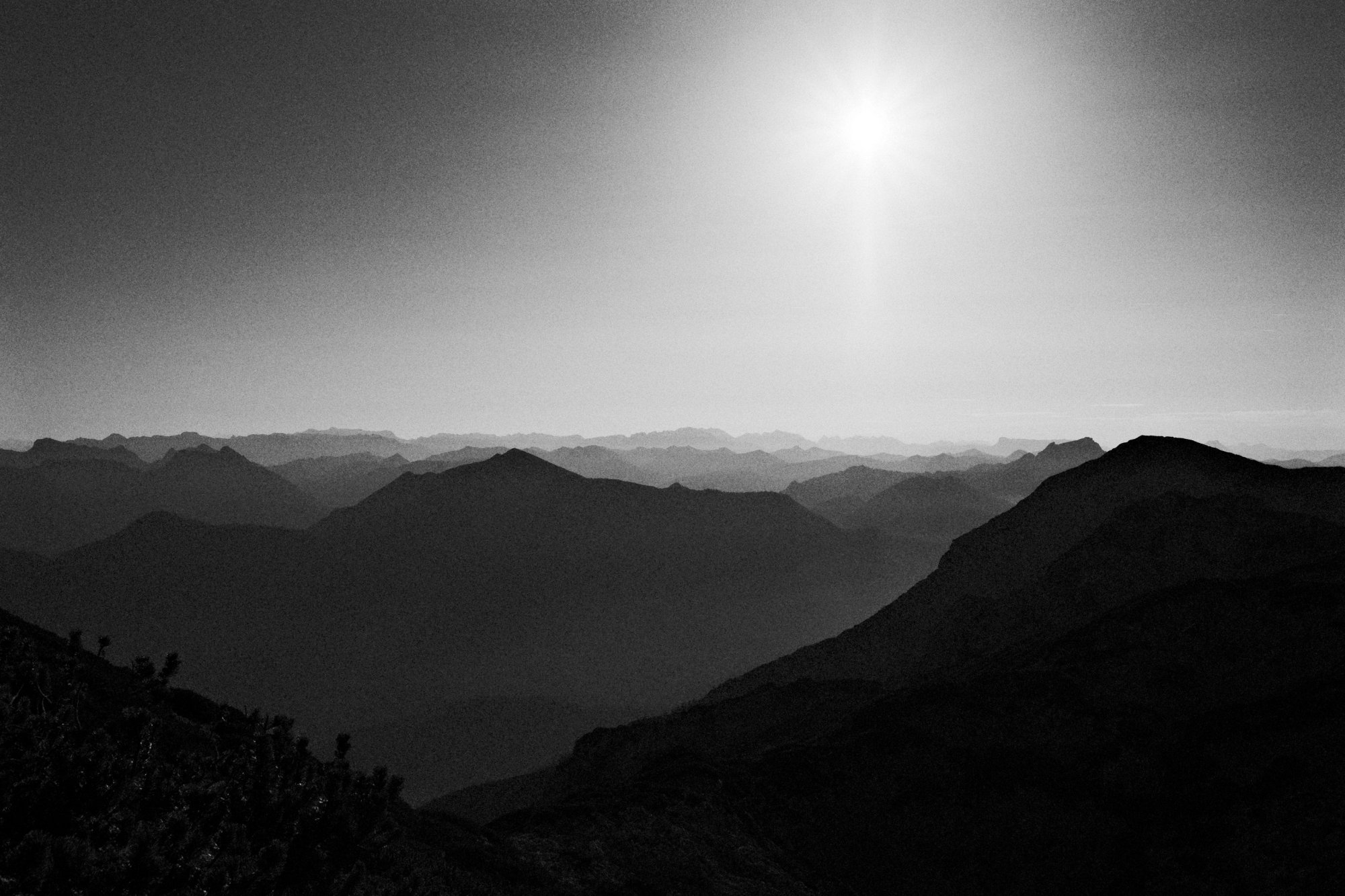 Schwarz-weiße Berglandschaft mit mehreren Gebirgsketten in Silhouette unter hellem Himmel.