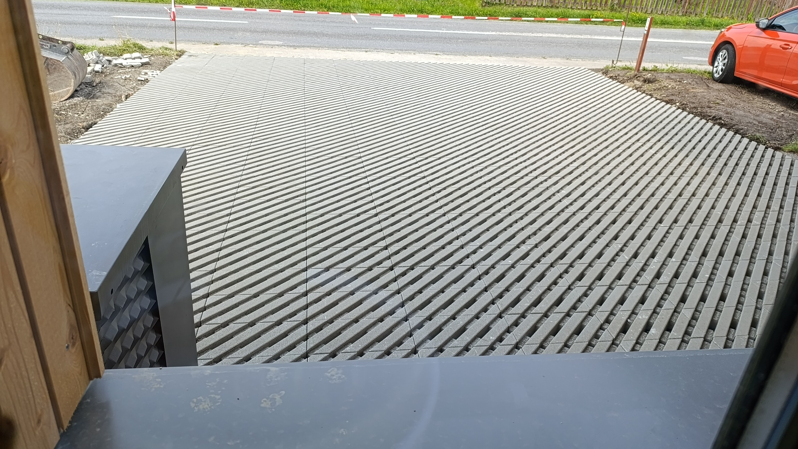 Metallische Bodengitterplatten auf einer Baustelle mit Straße und orangem Auto im Hintergrund.